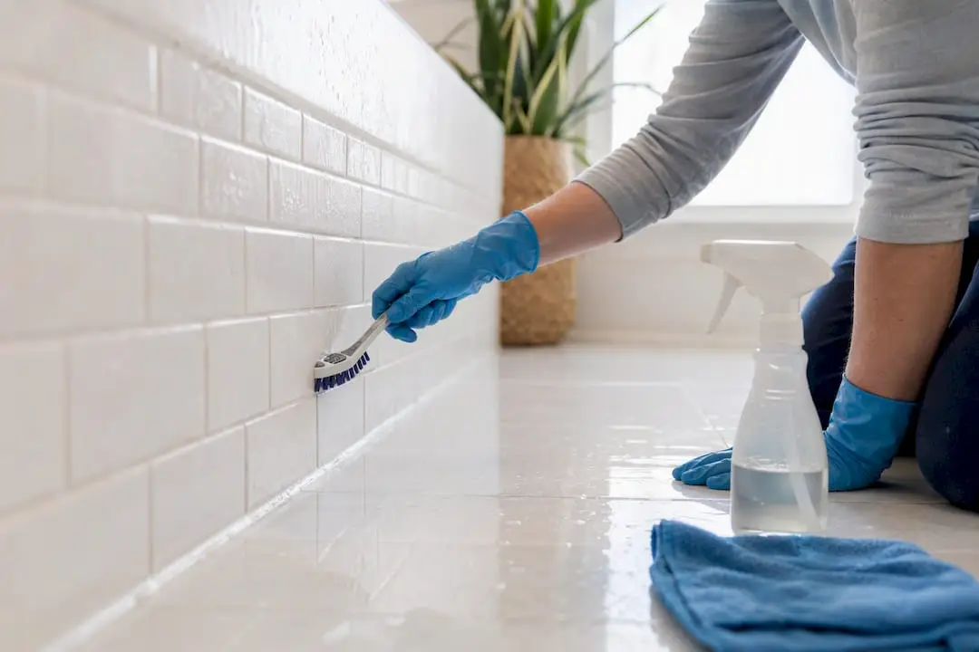 Hands scrubbing bathroom grout near tub