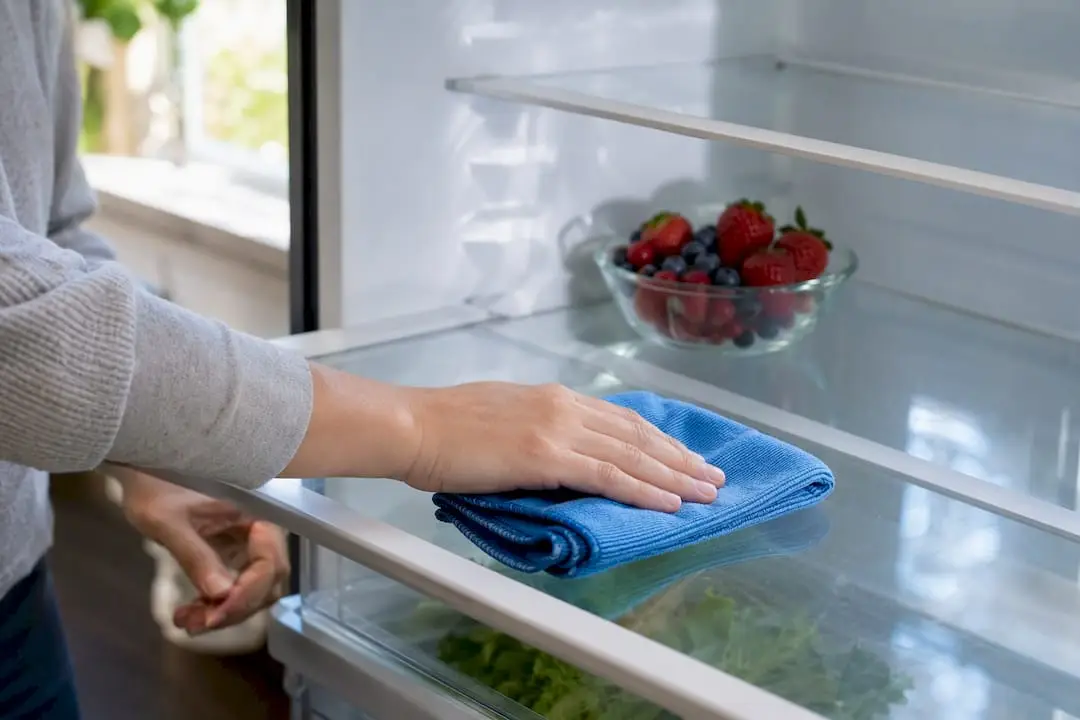 Hands wiping an organized refrigerator shelf